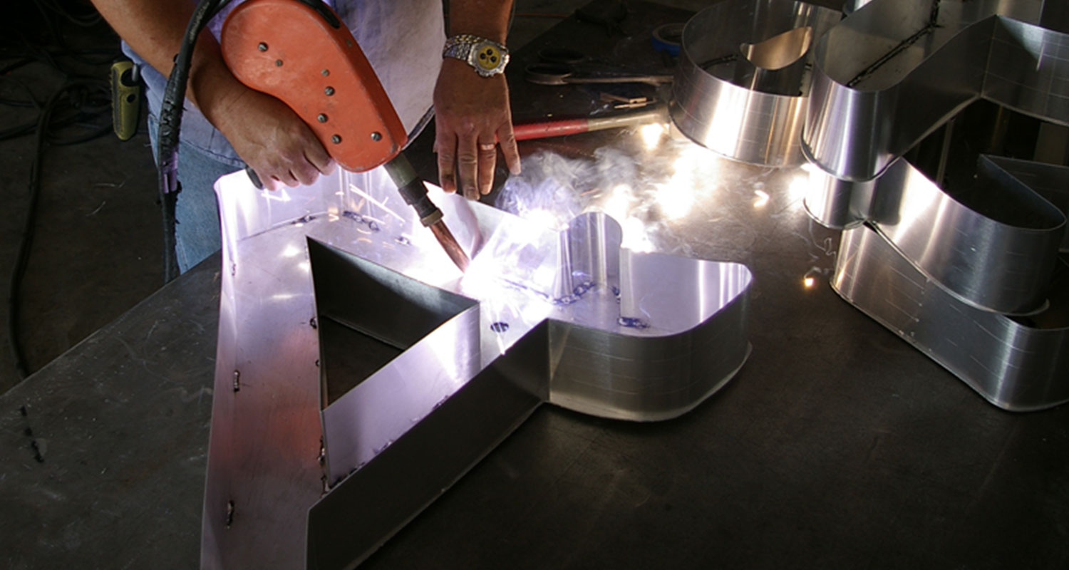 Craftsman welding a metal channel letter sign for commercial use.